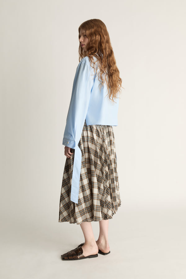 Woman wearing a light blue shirt and plaid skirt on a plain background