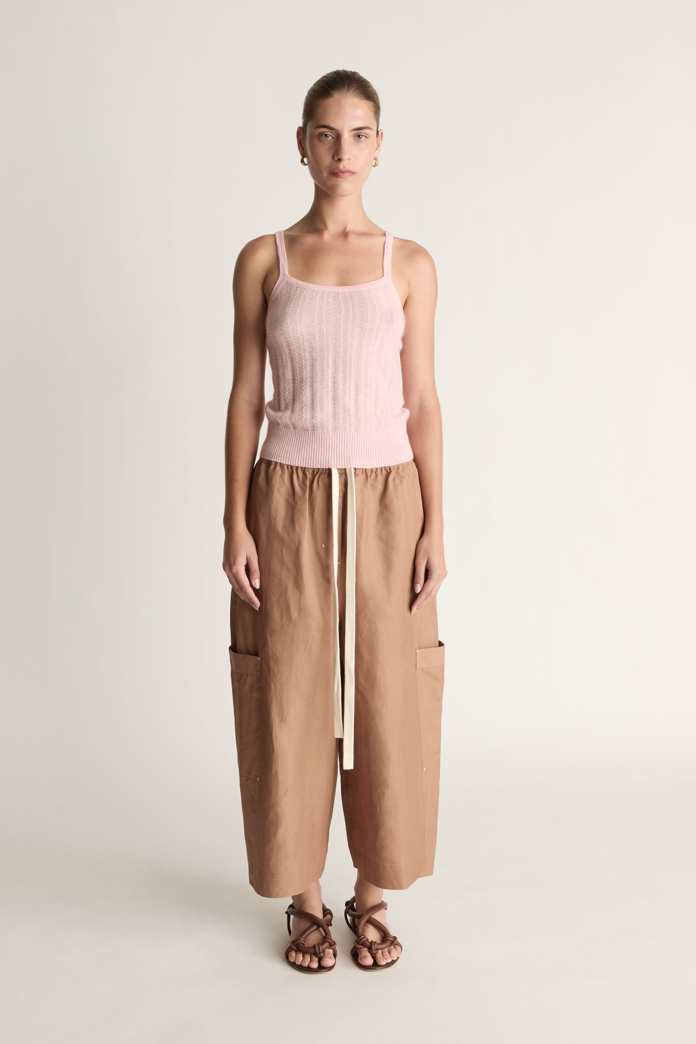 Woman wearing a pink top and brown pants on a white background