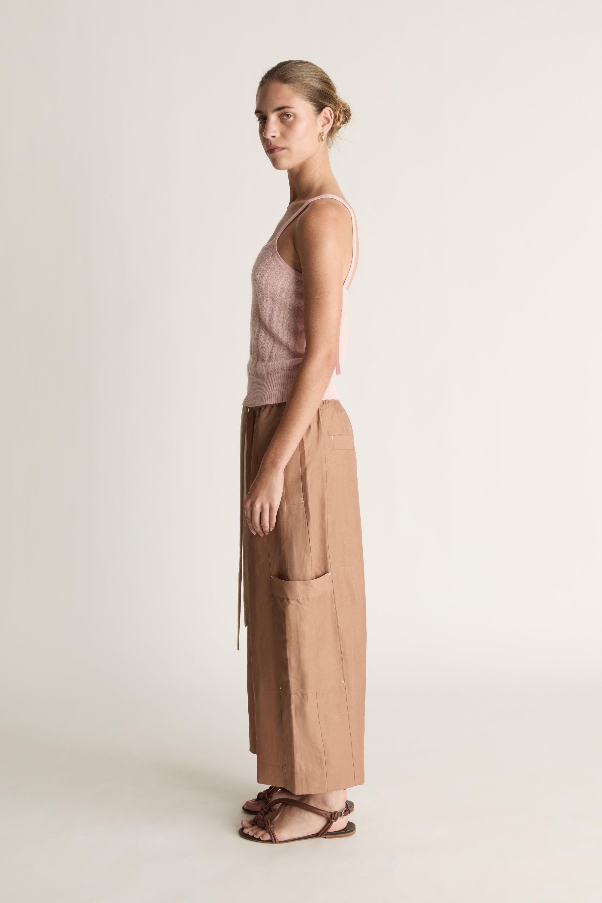 Woman wearing a pink top and brown pants on a white background