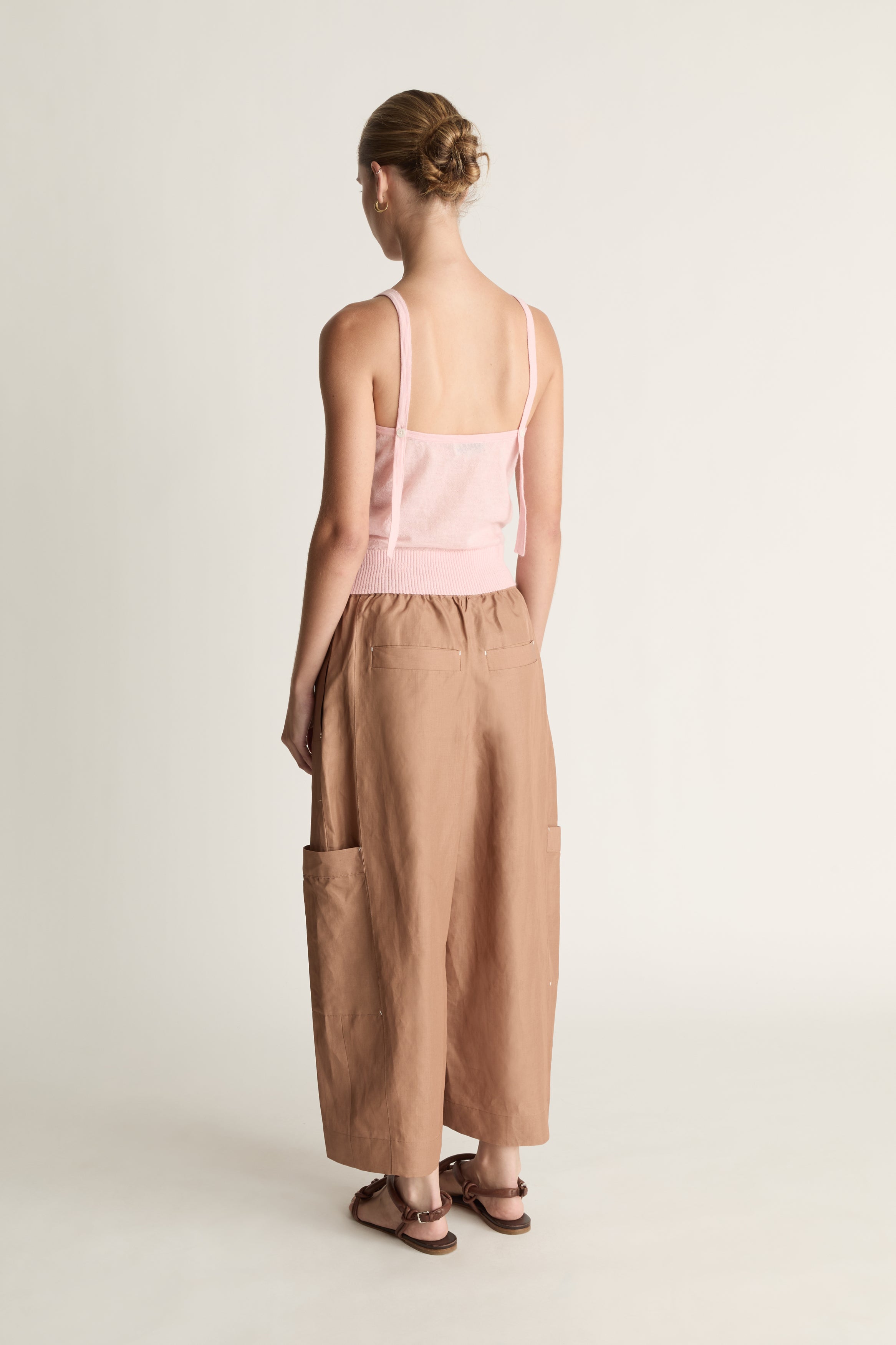 Woman wearing a pink top and brown pants on a white background