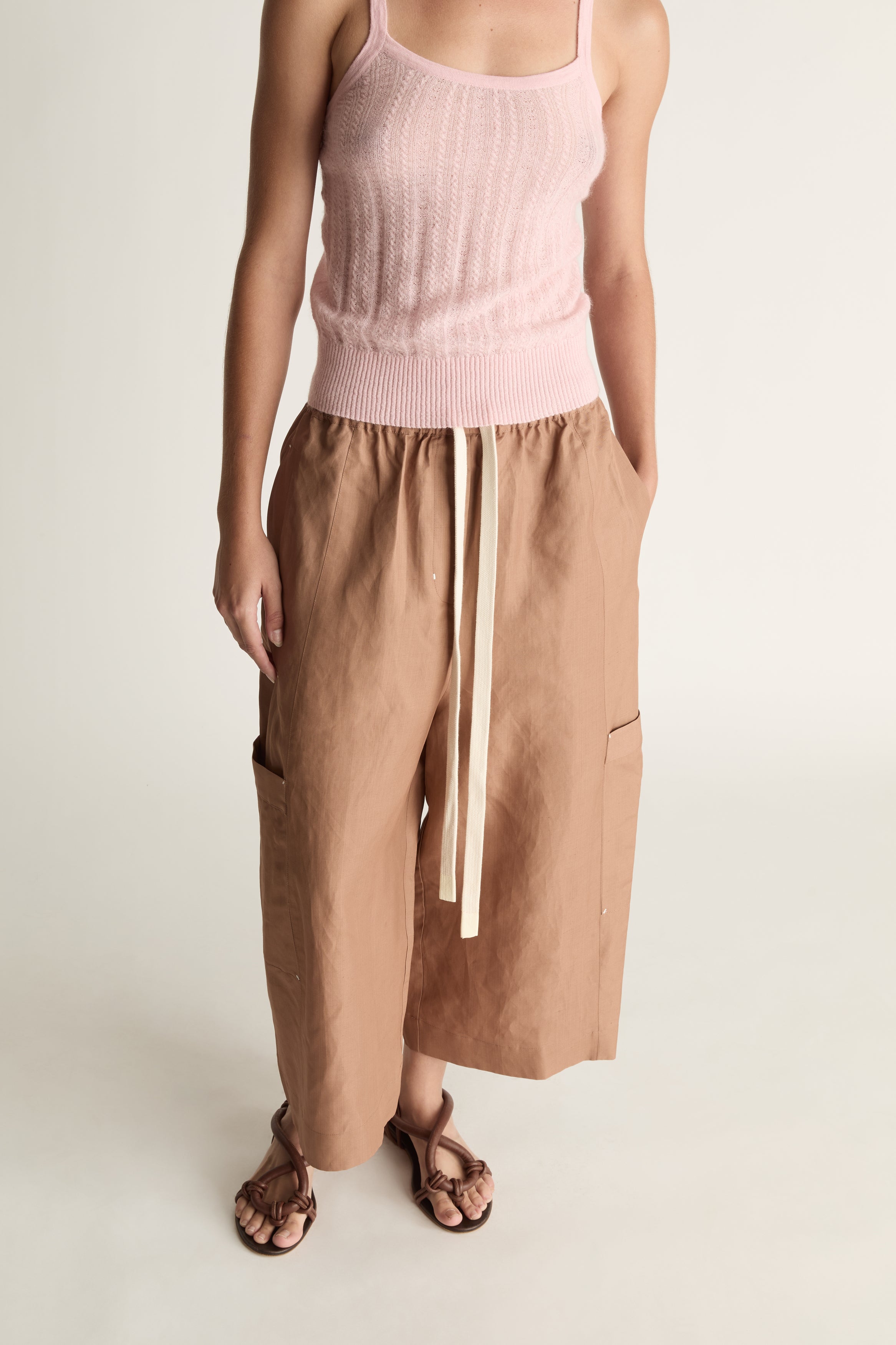 Woman wearing a pink top and brown pants on a white background