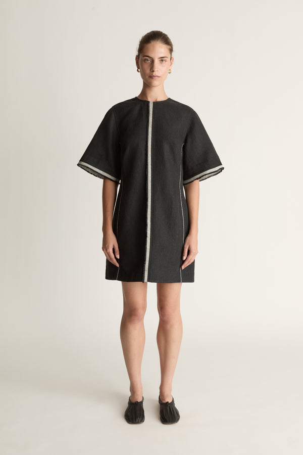 Black dress with white trim worn by a model on a light background