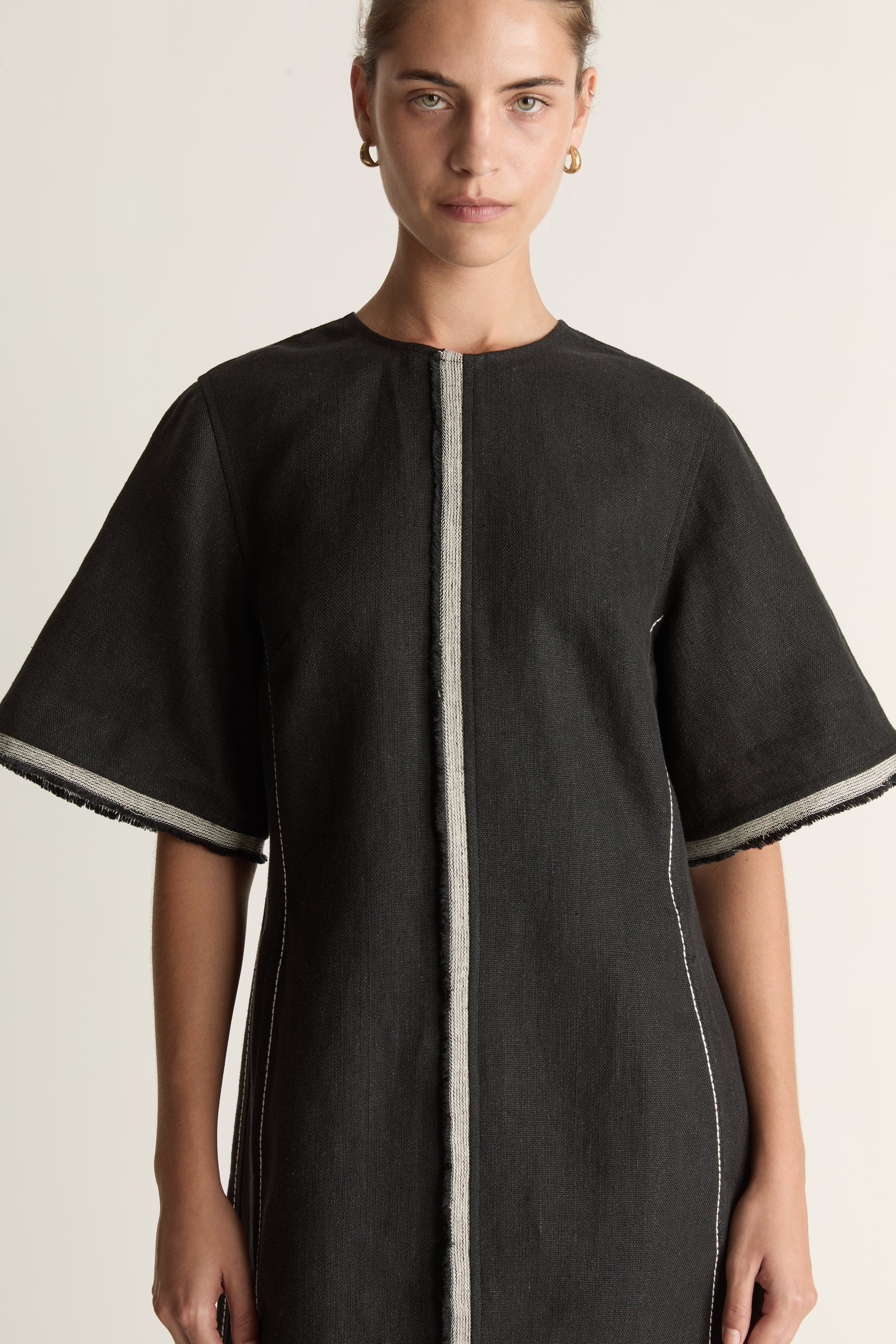 Black dress with white trim worn by a model on a light background