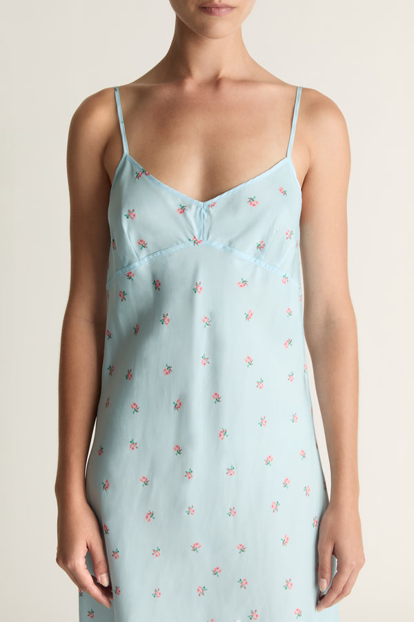Woman wearing a light blue slip dress with a subtle pattern on a plain background