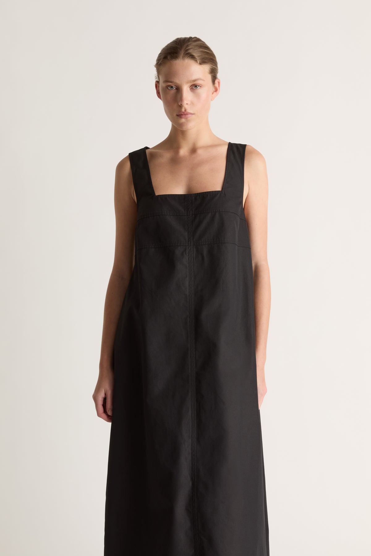 Close-up front view of a black dress with a square neckline, wide straps and topstitched seams.