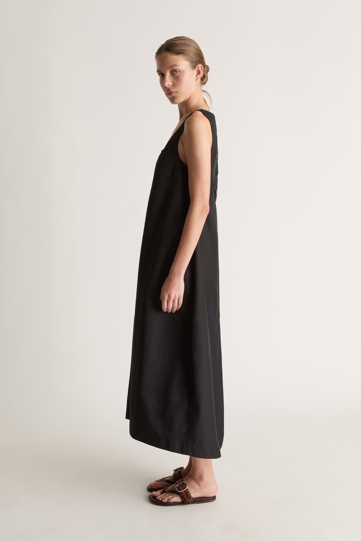 Side view of a sleeveless black midi dress with wide straps and a loose A-line shape.