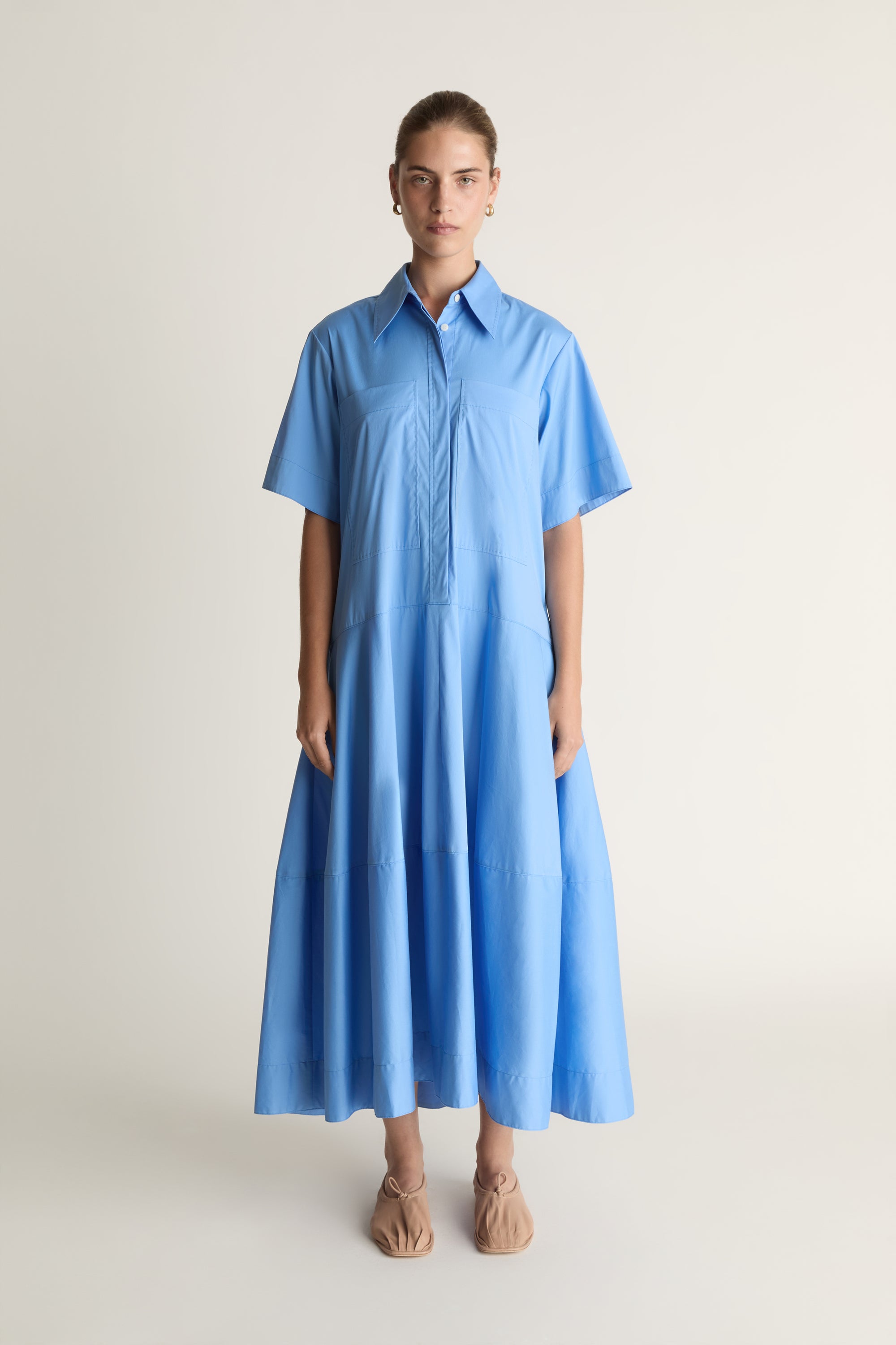 A woman wearing a blue shirt dress against a plain background