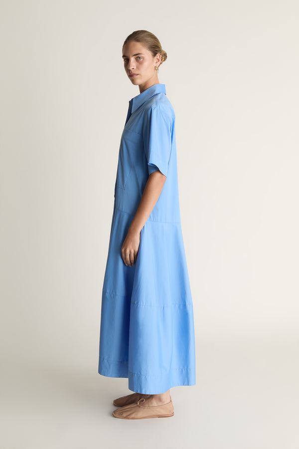 A woman wearing a blue shirt dress against a plain background