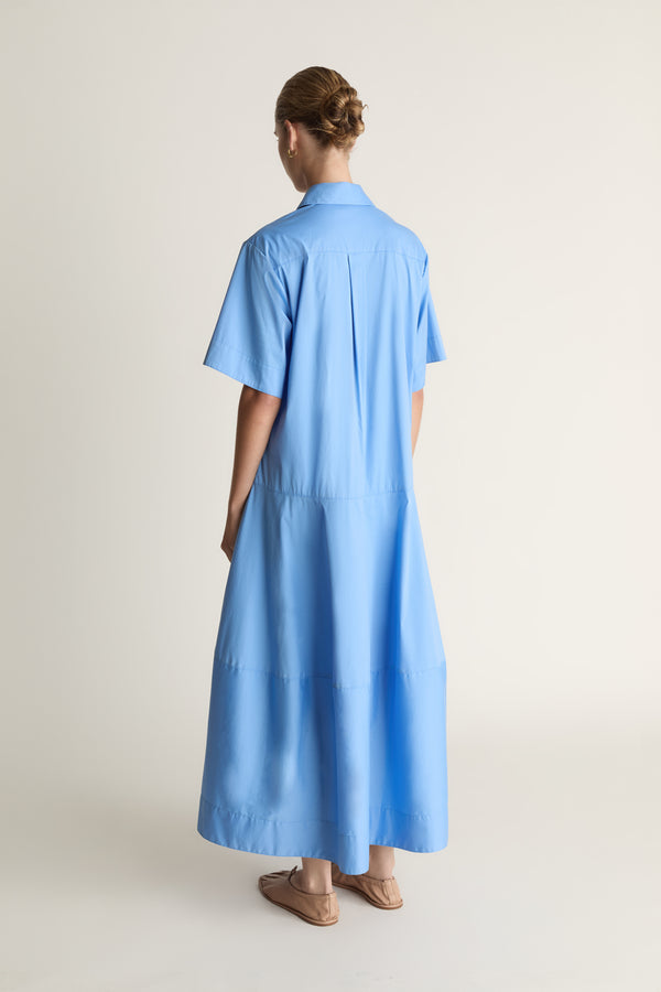 A woman wearing a blue shirt dress against a plain background