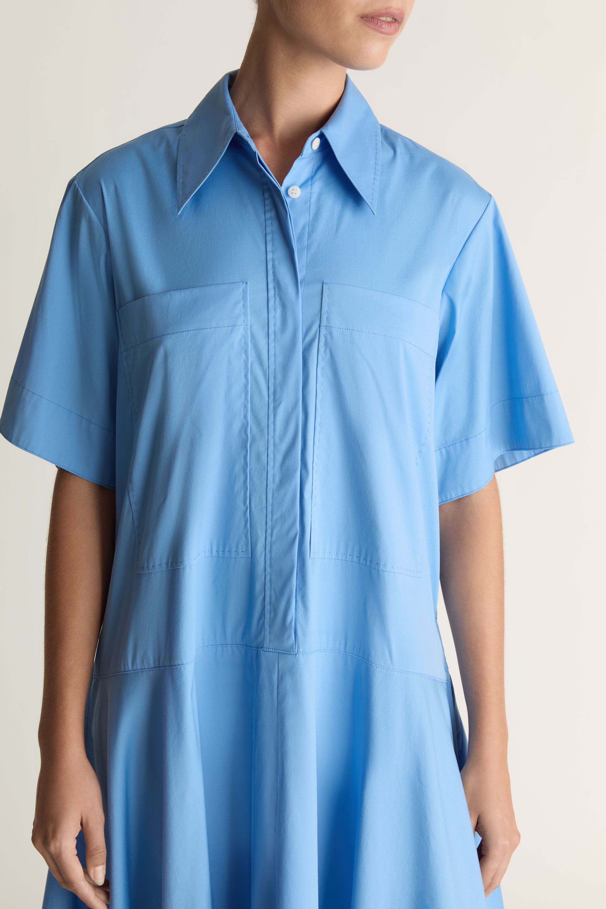 A woman wearing a blue shirt dress against a plain background