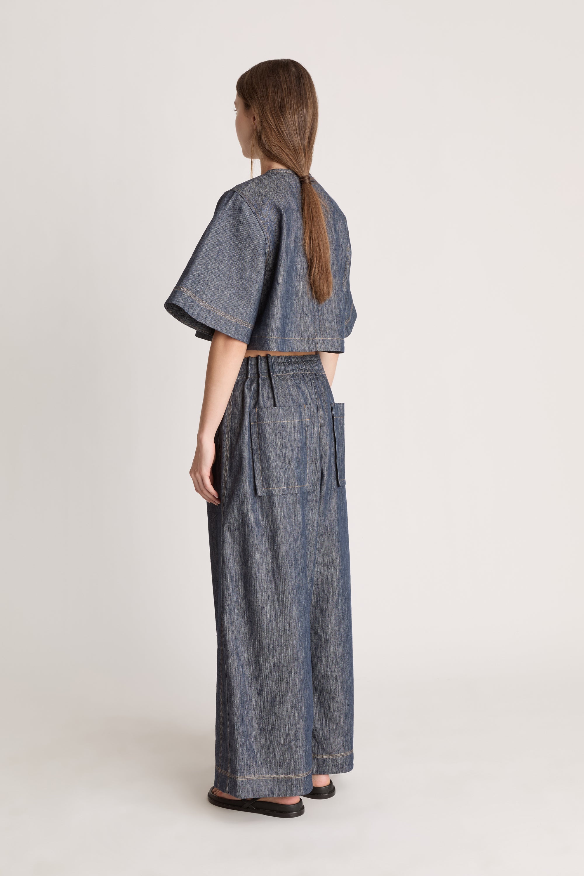 Woman wearing a denim outfit with wide-leg pants and a cropped top on a white background