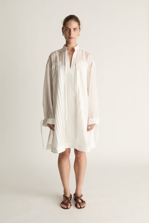 Woman wearing a white tunic against a plain background