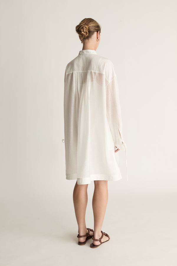 Woman wearing a white tunic against a plain background