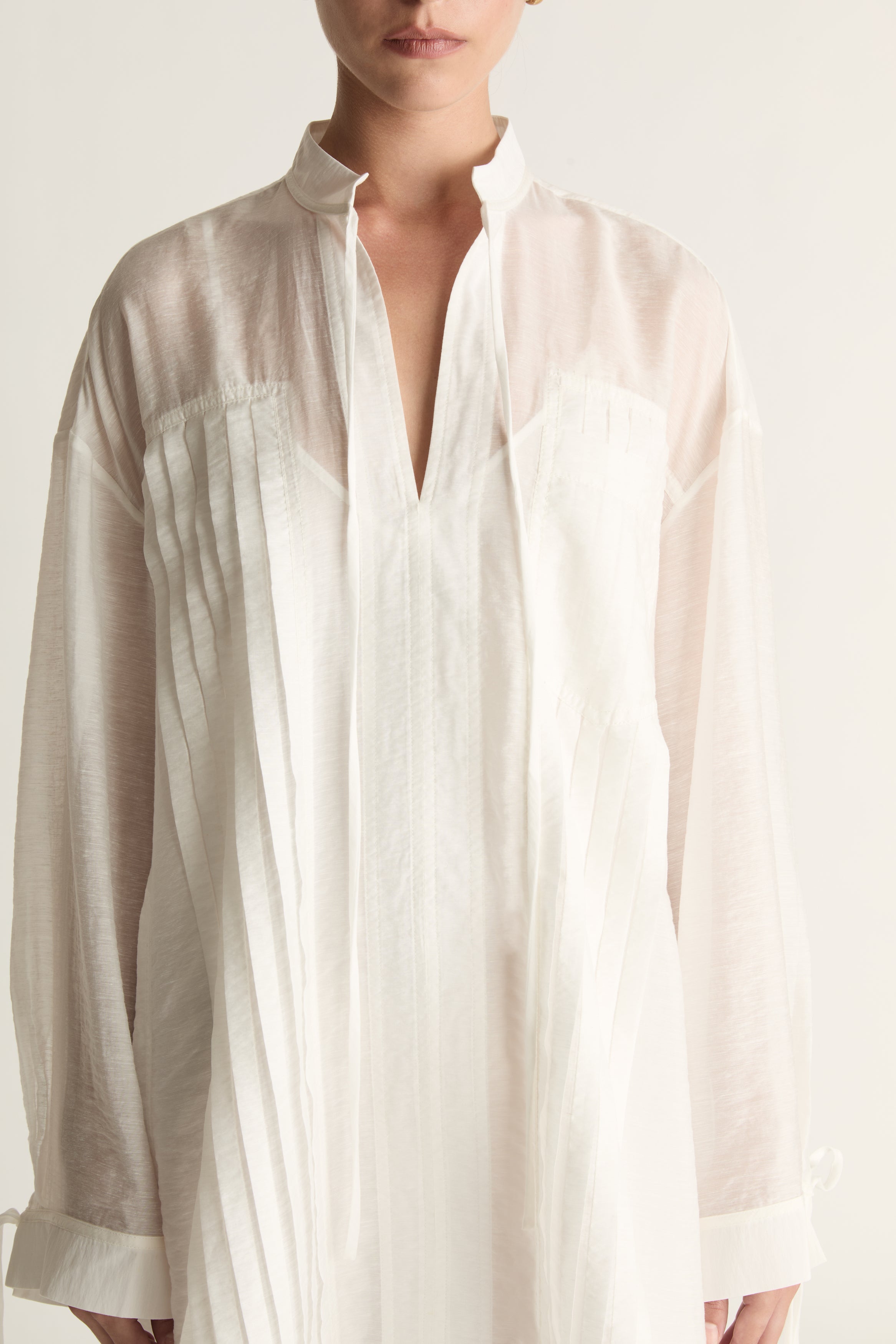 Woman wearing a white tunic against a plain background