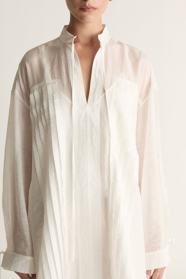 Woman wearing a white tunic against a plain background