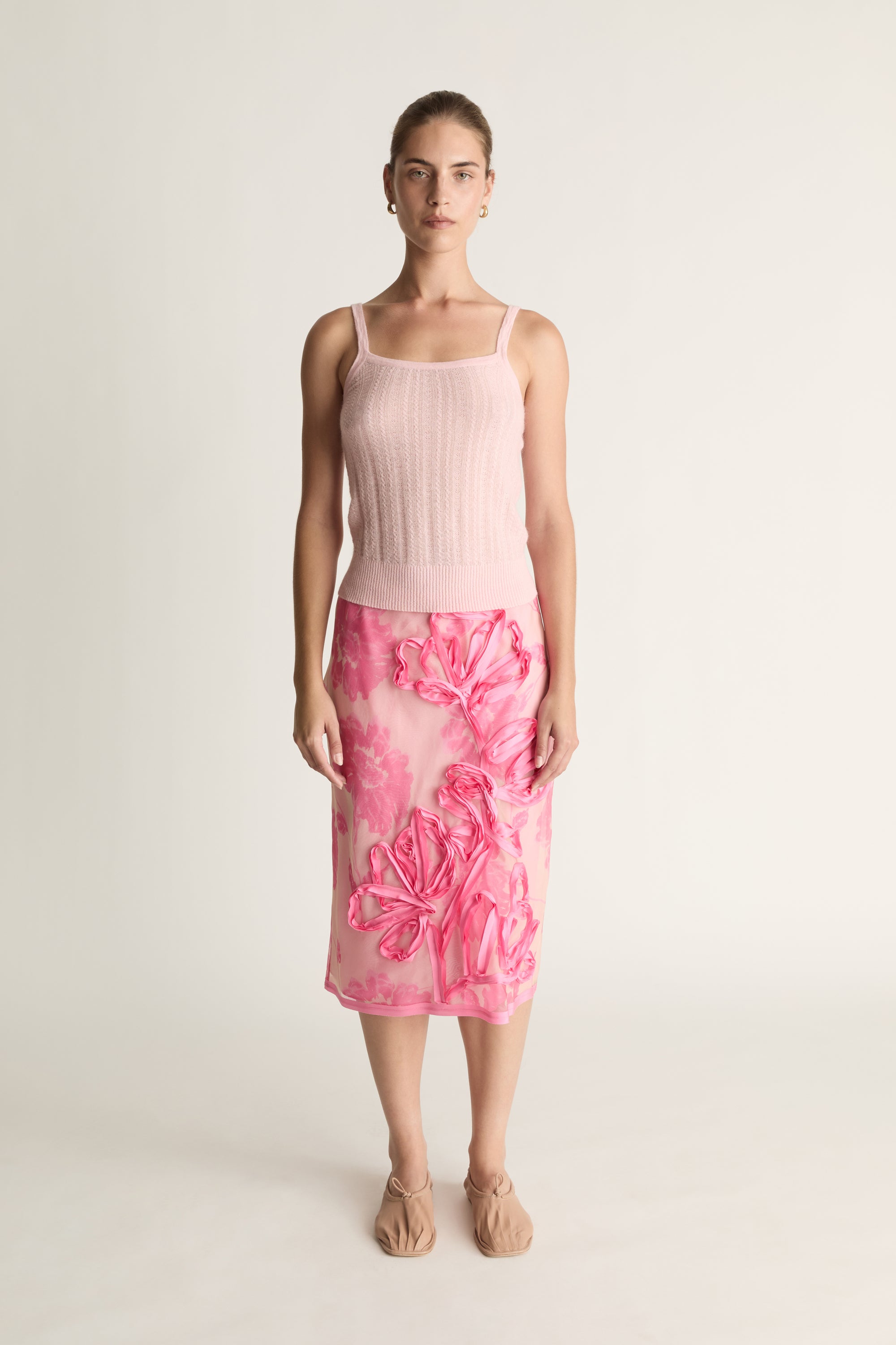 Woman wearing a pink tank top and floral skirt on a white background