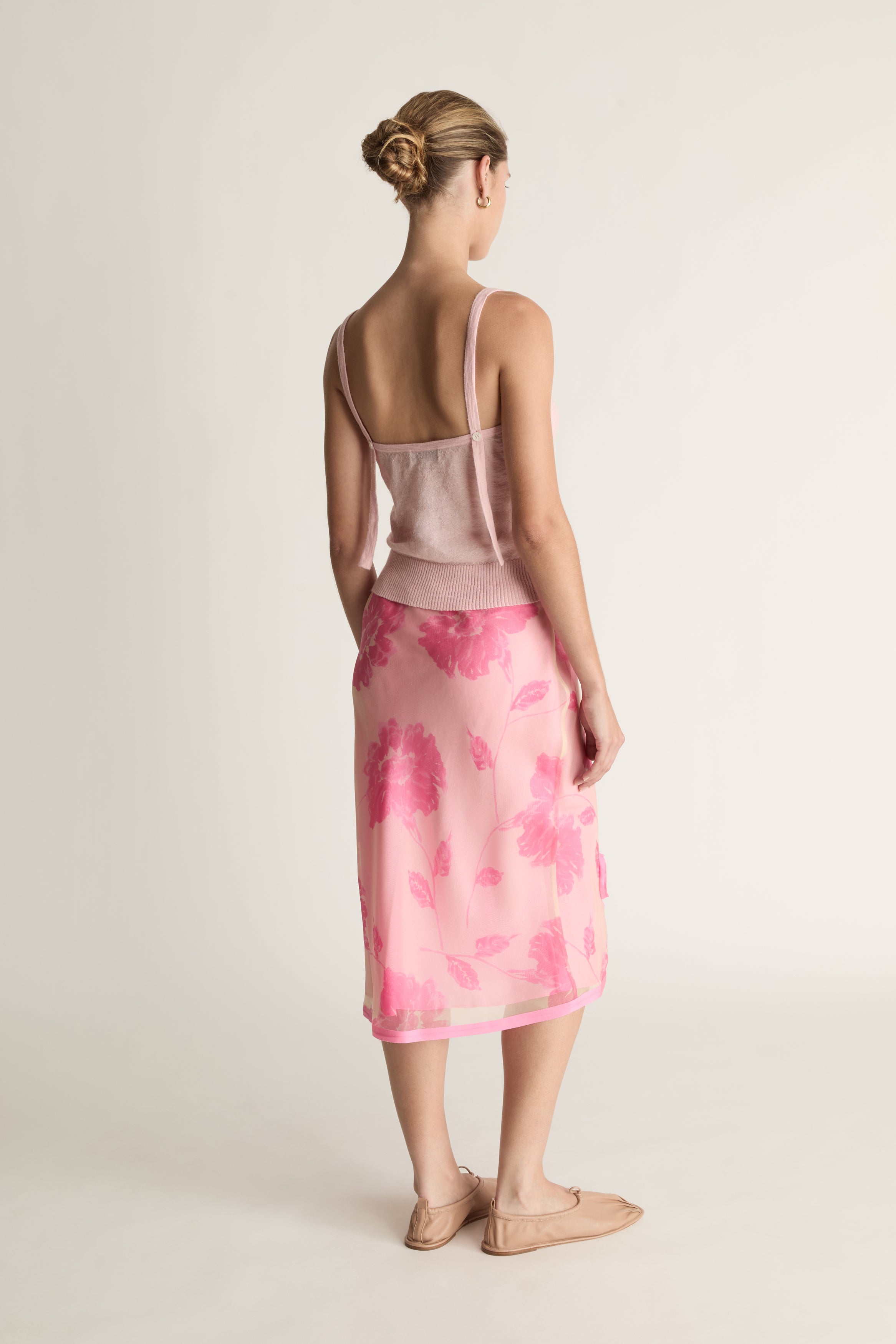 Woman wearing a pink top and pink floral  against a plain background