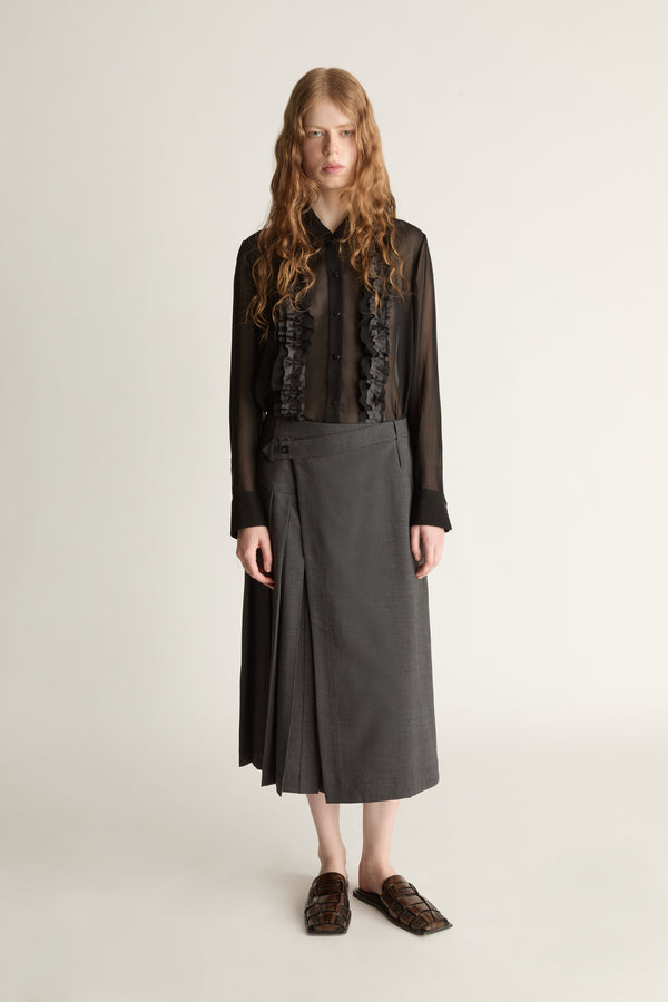 Person wearing a black blouse with lace details and a gray pleated skirt on a white background