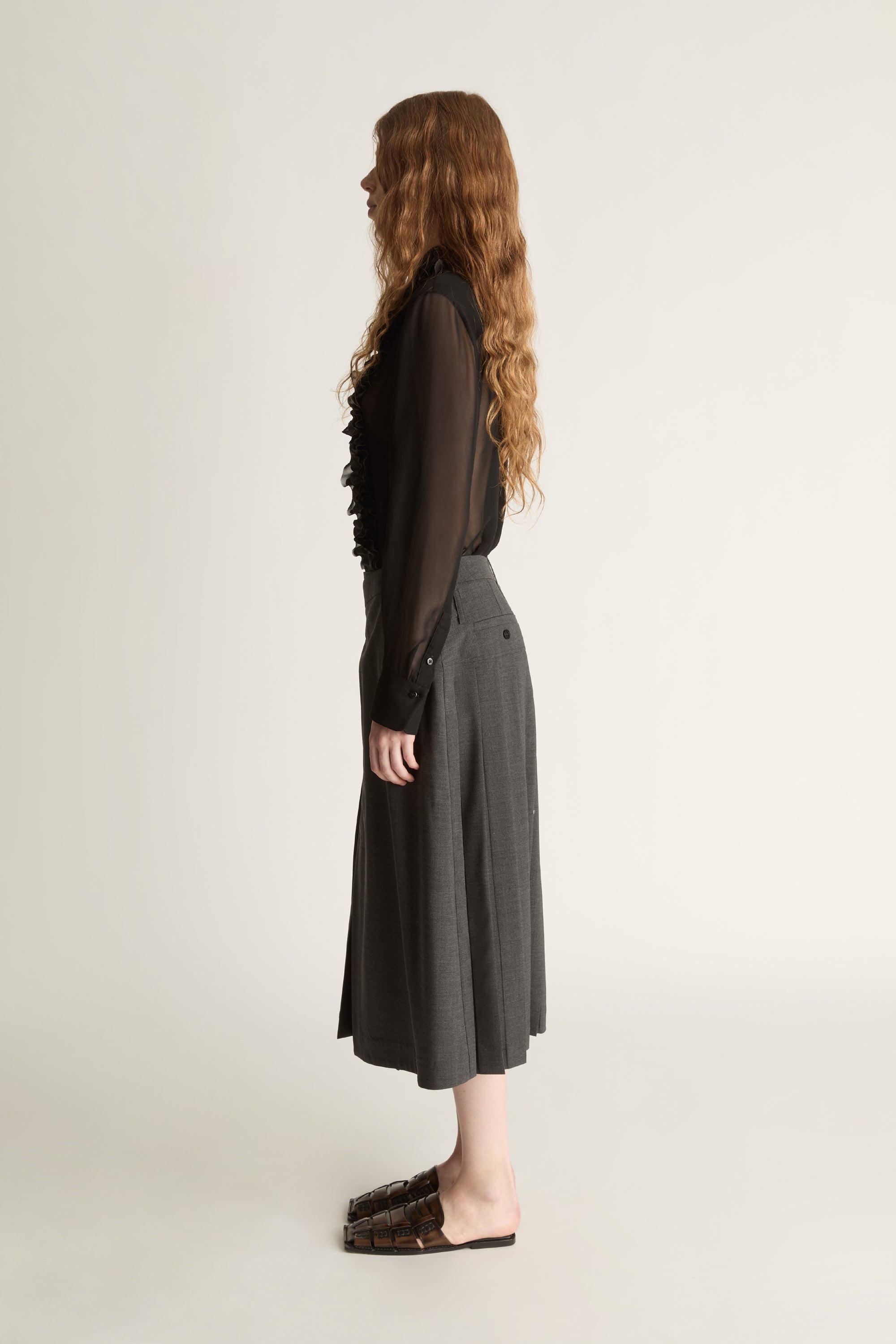 Person wearing a black blouse with lace details and a gray pleated skirt on a white background
