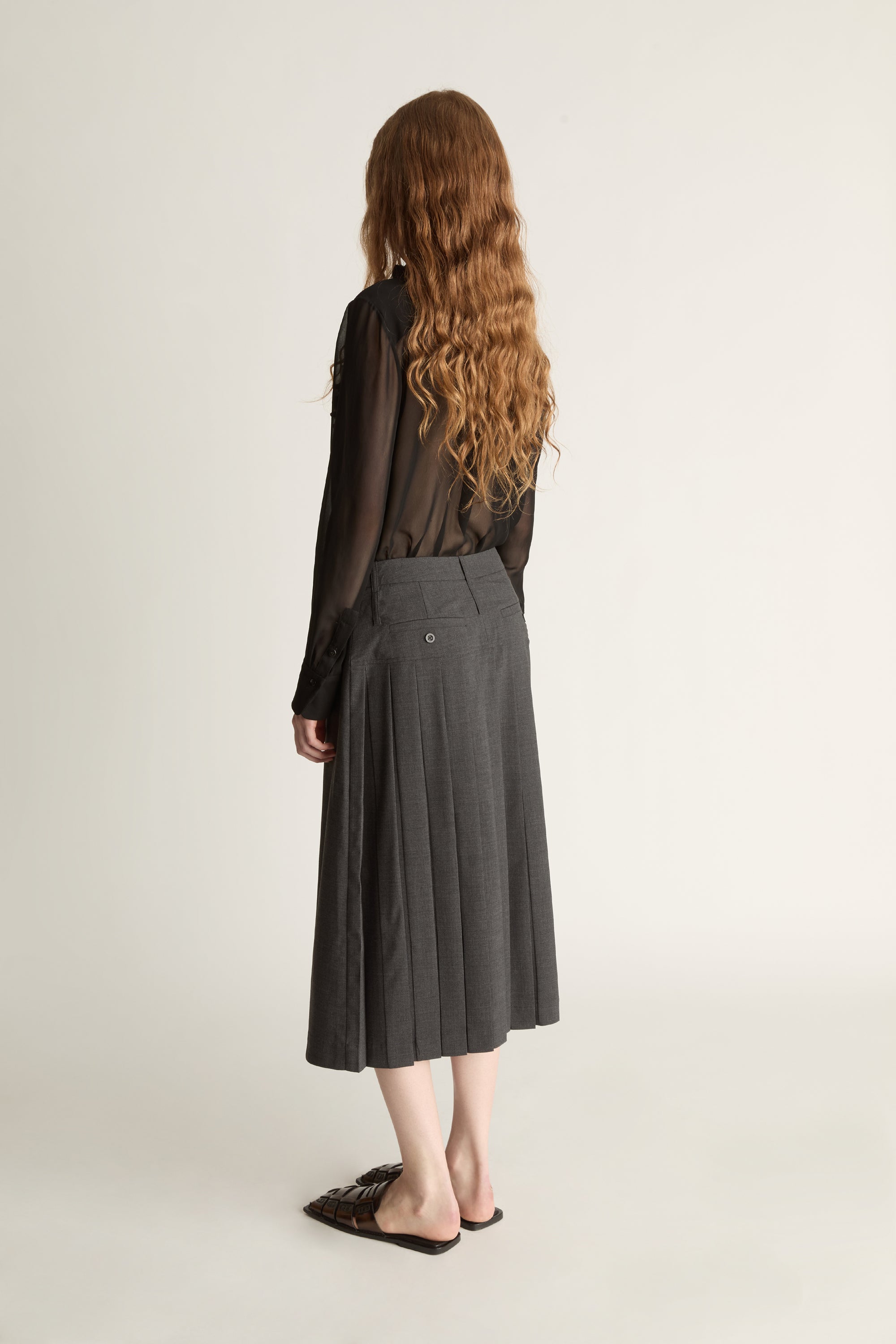 Person wearing a black blouse with lace details and a gray pleated skirt on a white background