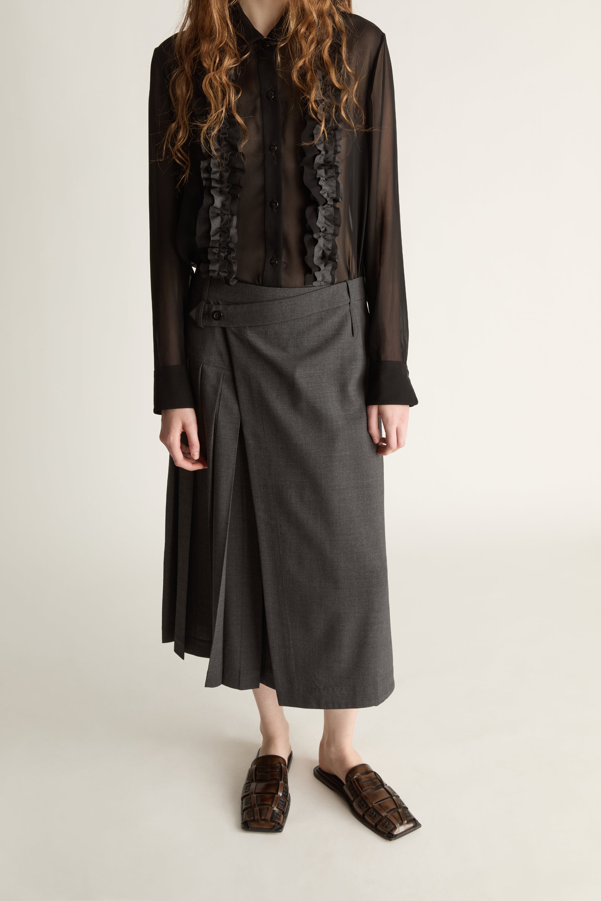 Person wearing a black blouse with lace details and a gray pleated skirt on a white background