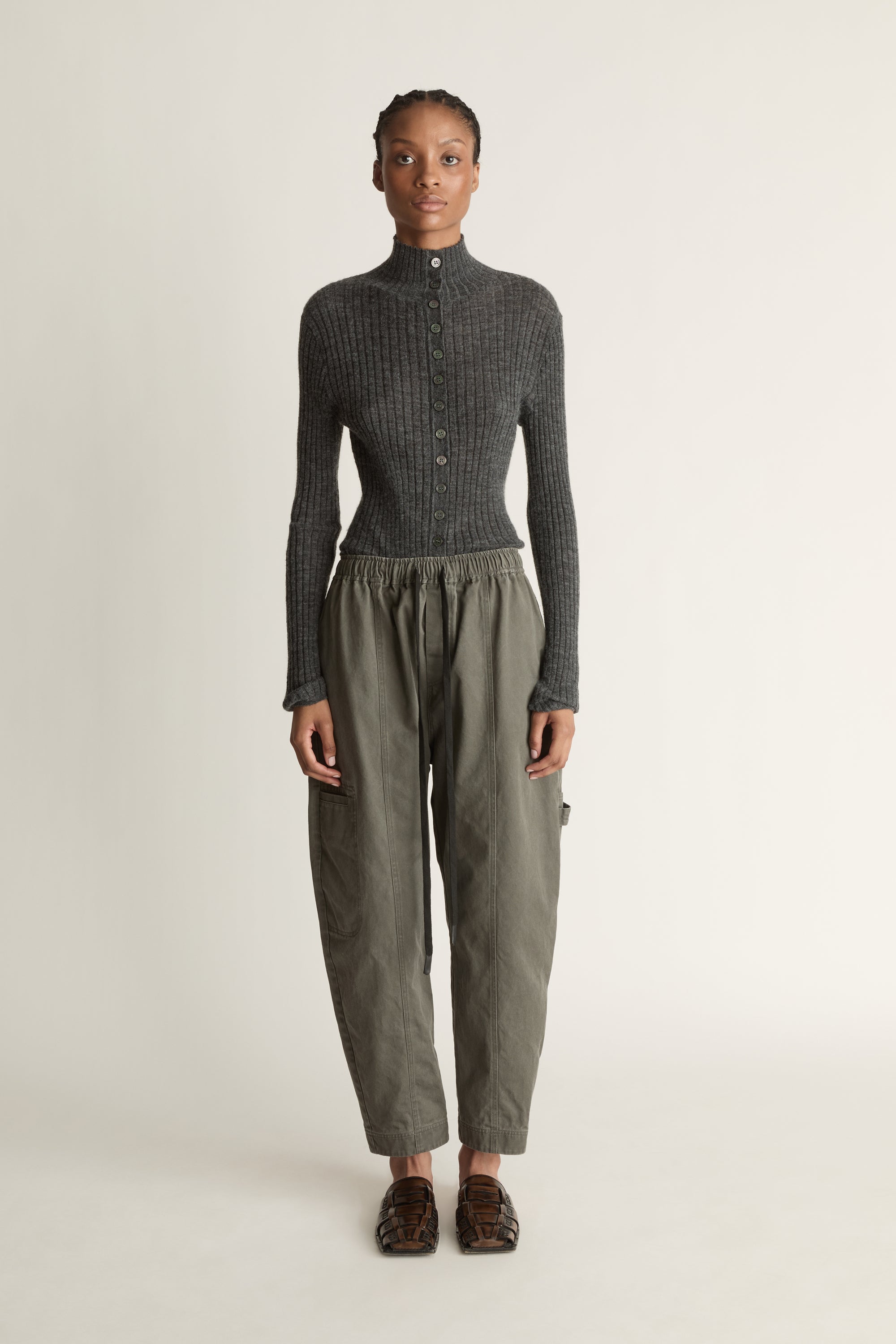 Person wearing a dark gray ribbed long-sleeve top and light gray pants on a white background