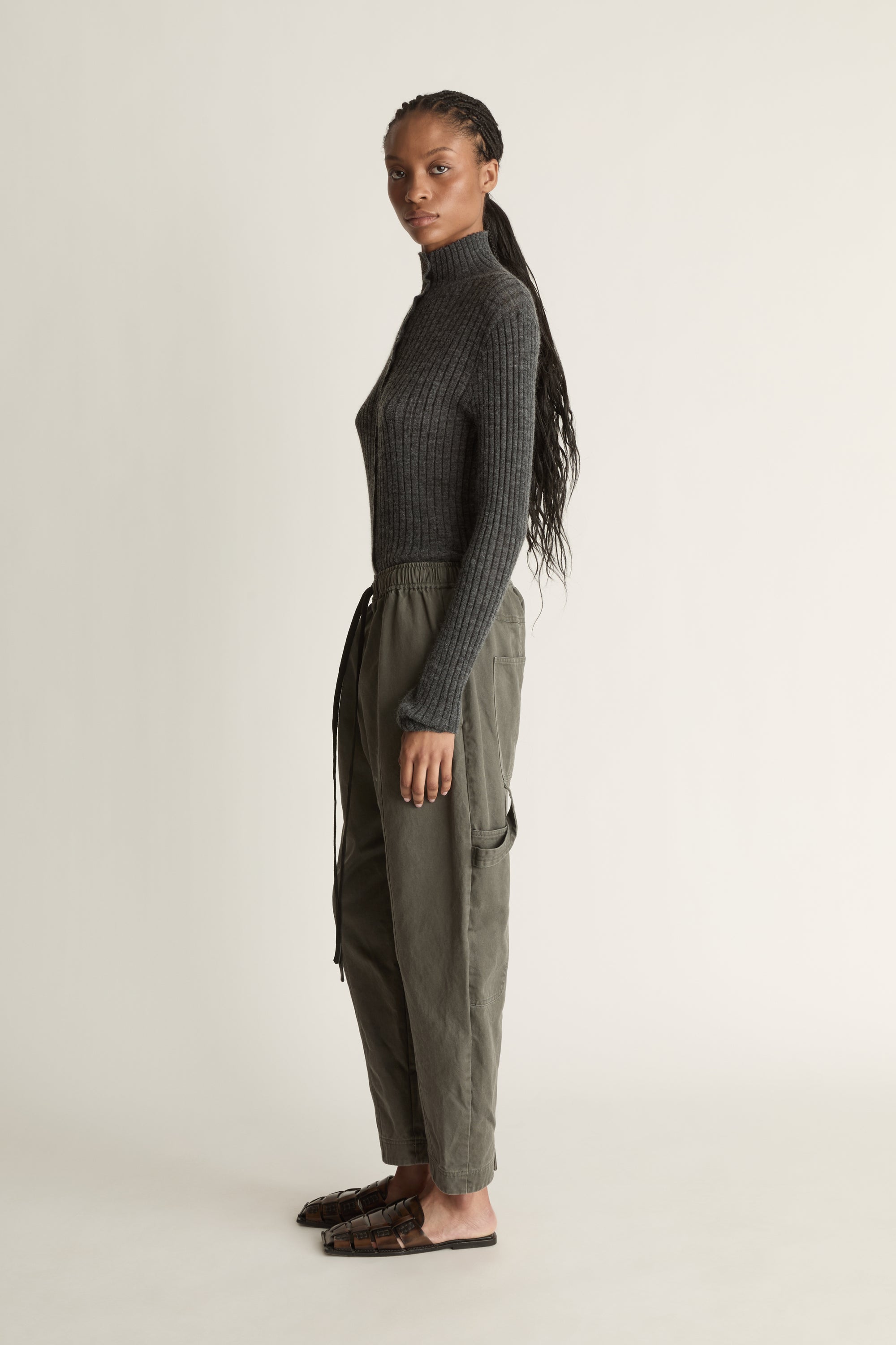 Person wearing a dark gray ribbed long-sleeve top and light gray pants on a white background