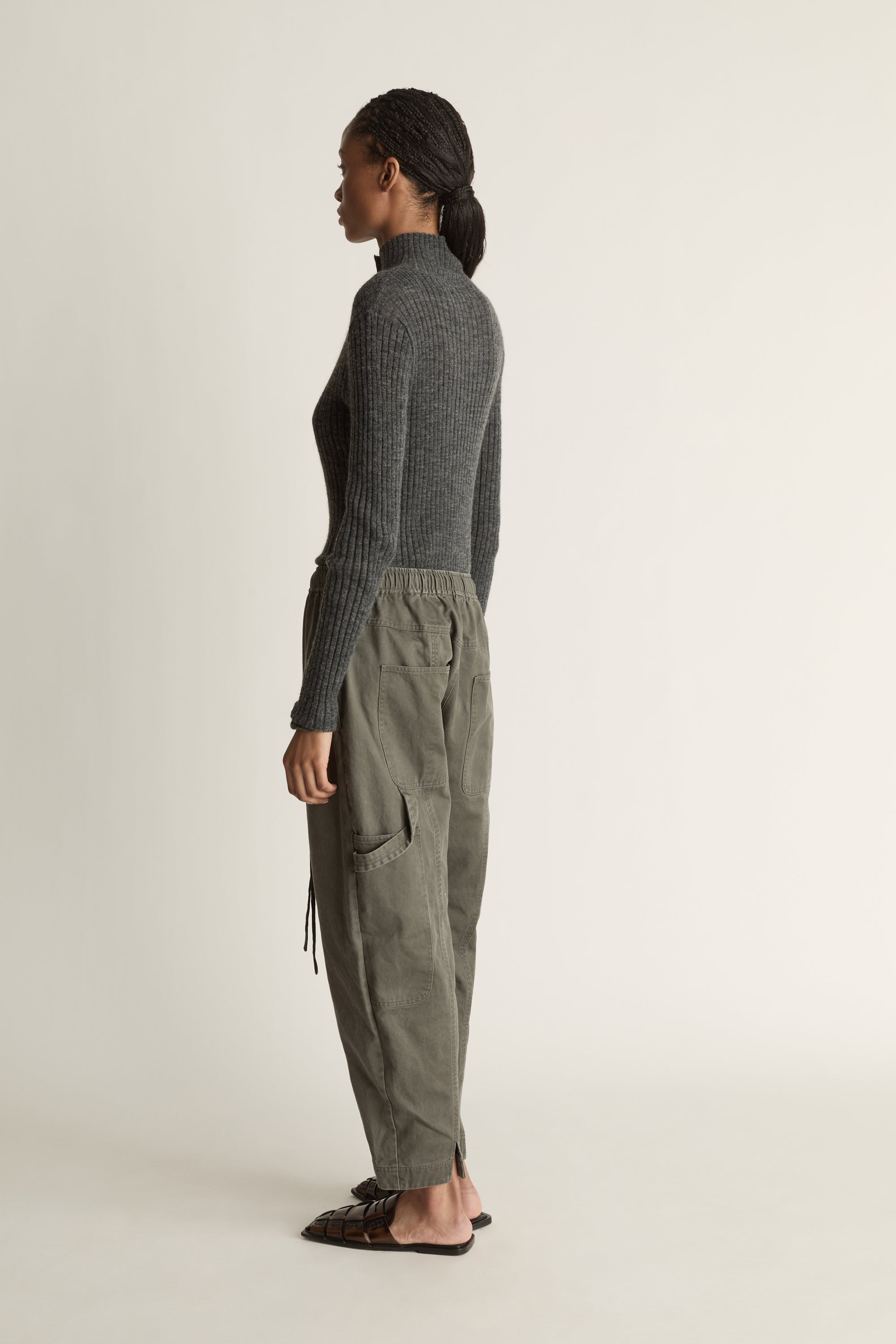 Person wearing a dark gray ribbed long-sleeve top and light gray pants on a white background