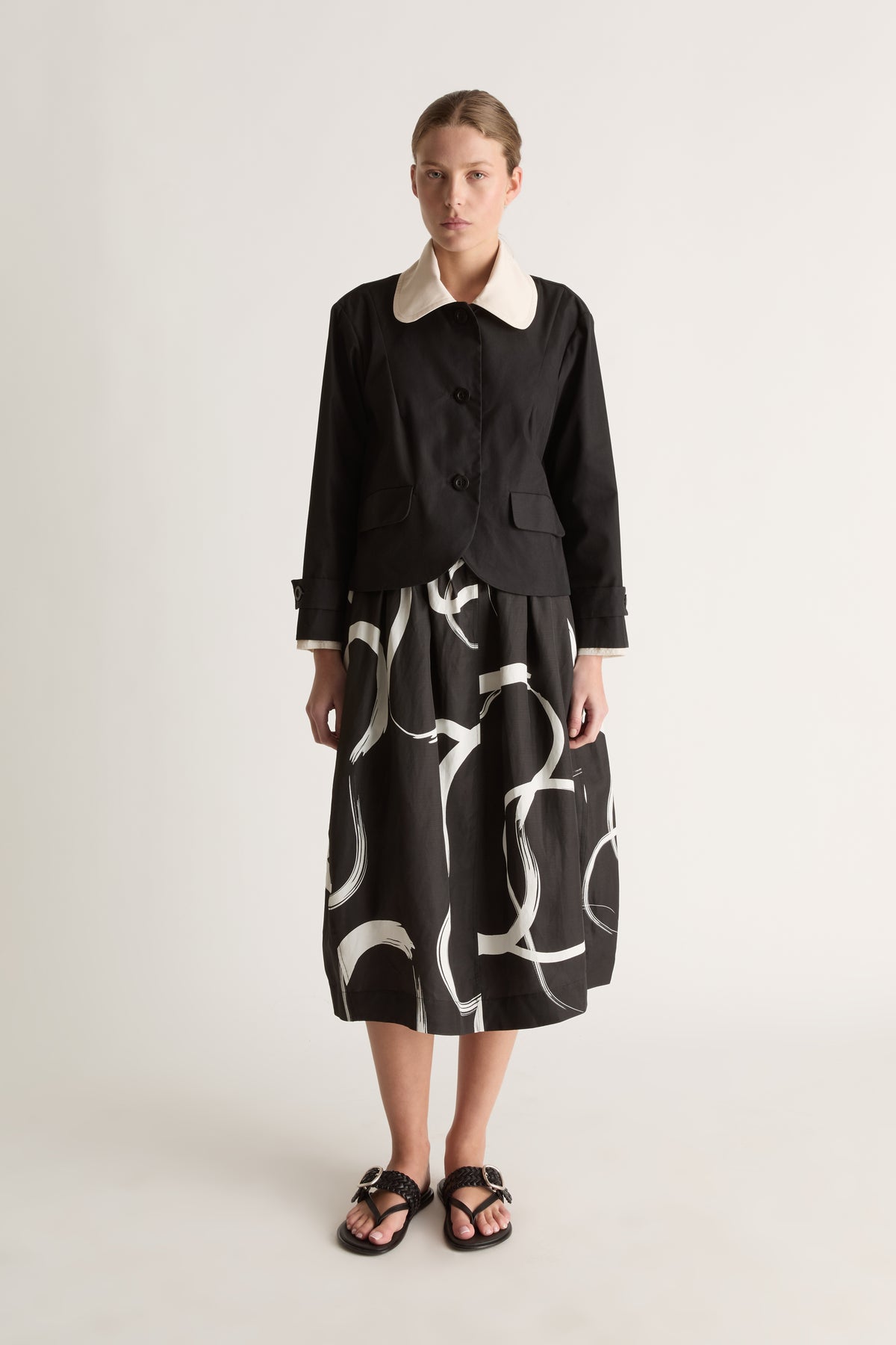 Front view of a cropped black jacket with a rounded cream collar, three-button front, flap pockets and tabbed cuffs.