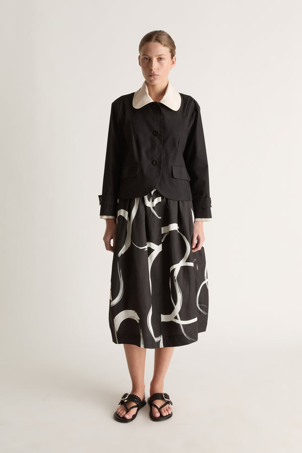 Front view of a cropped black jacket with a rounded cream collar, three-button front, flap pockets and tabbed cuffs.