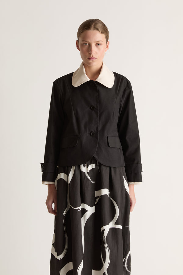 Close-up front view of a black jacket with a rounded cream collar, button front and flap pockets.