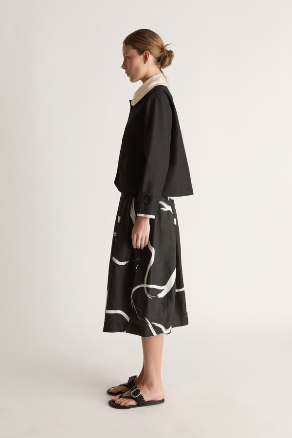 Side view of a cropped black jacket with a cream collar and boxy shape, worn over a printed skirt.
