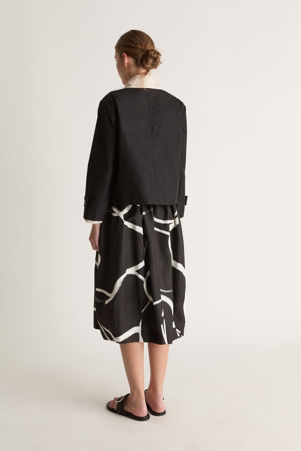 Back view of a cropped black jacket with a cream collar and a plain, boxy back.