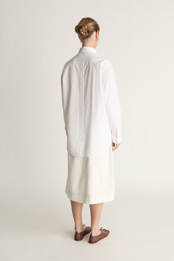 Person wearing a long white shirt and skirt on a plain background