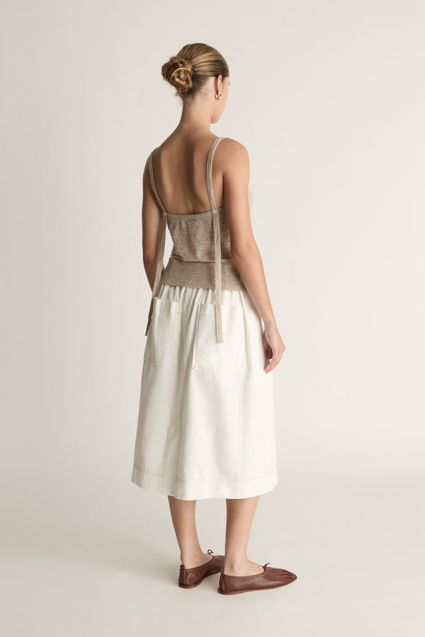 Woman wearing a beige tank top and white skirt on a plain background