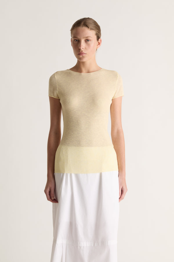 Close-up of a pale yellow sheer knit tee with round neckline, worn with a white skirt