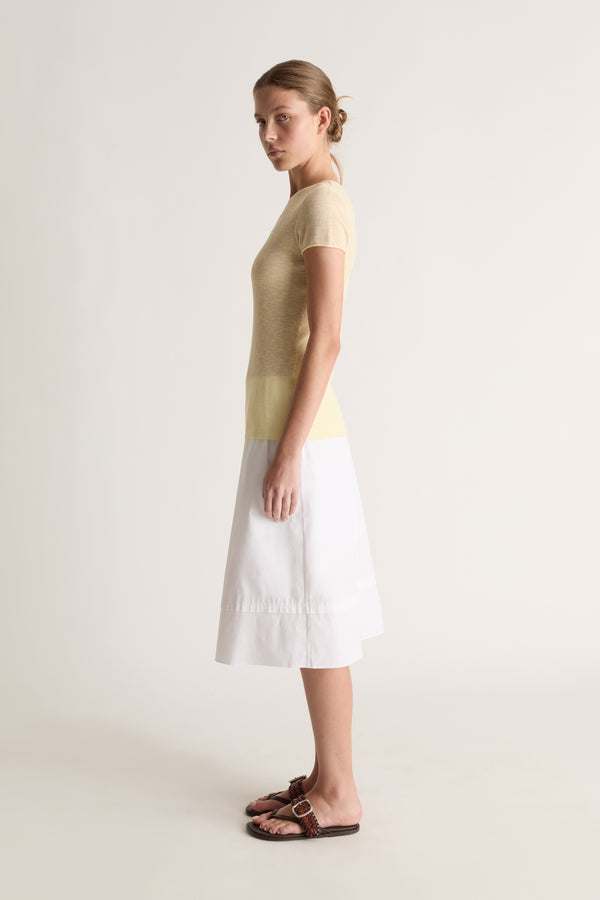 Side view of a woman with a bun in a pale yellow knit tee and white midi skirt with brown leather slides