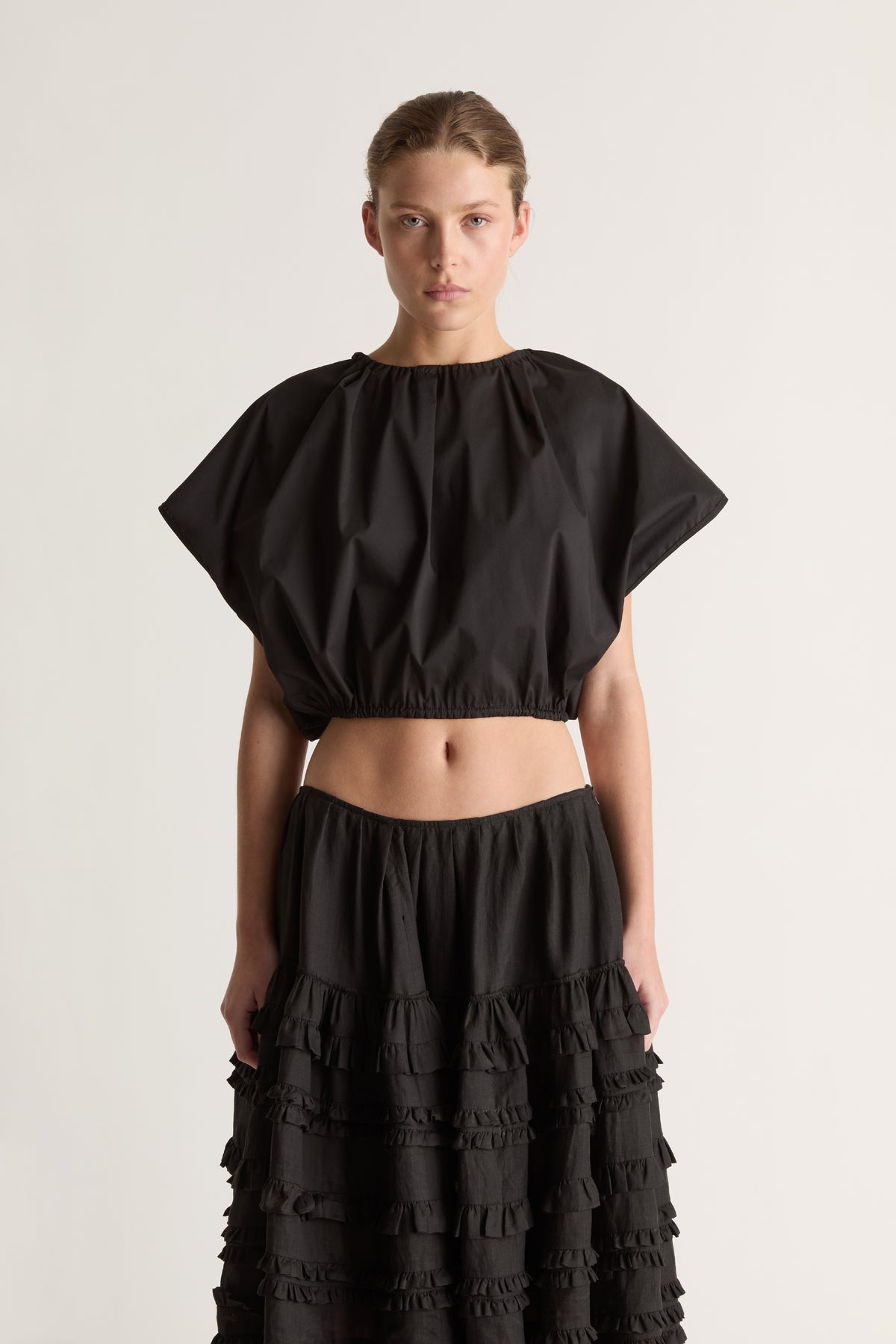 Close-up of a black short-sleeve cropped top with gathered neckline and hem, worn with a ruffle-tiered skirt