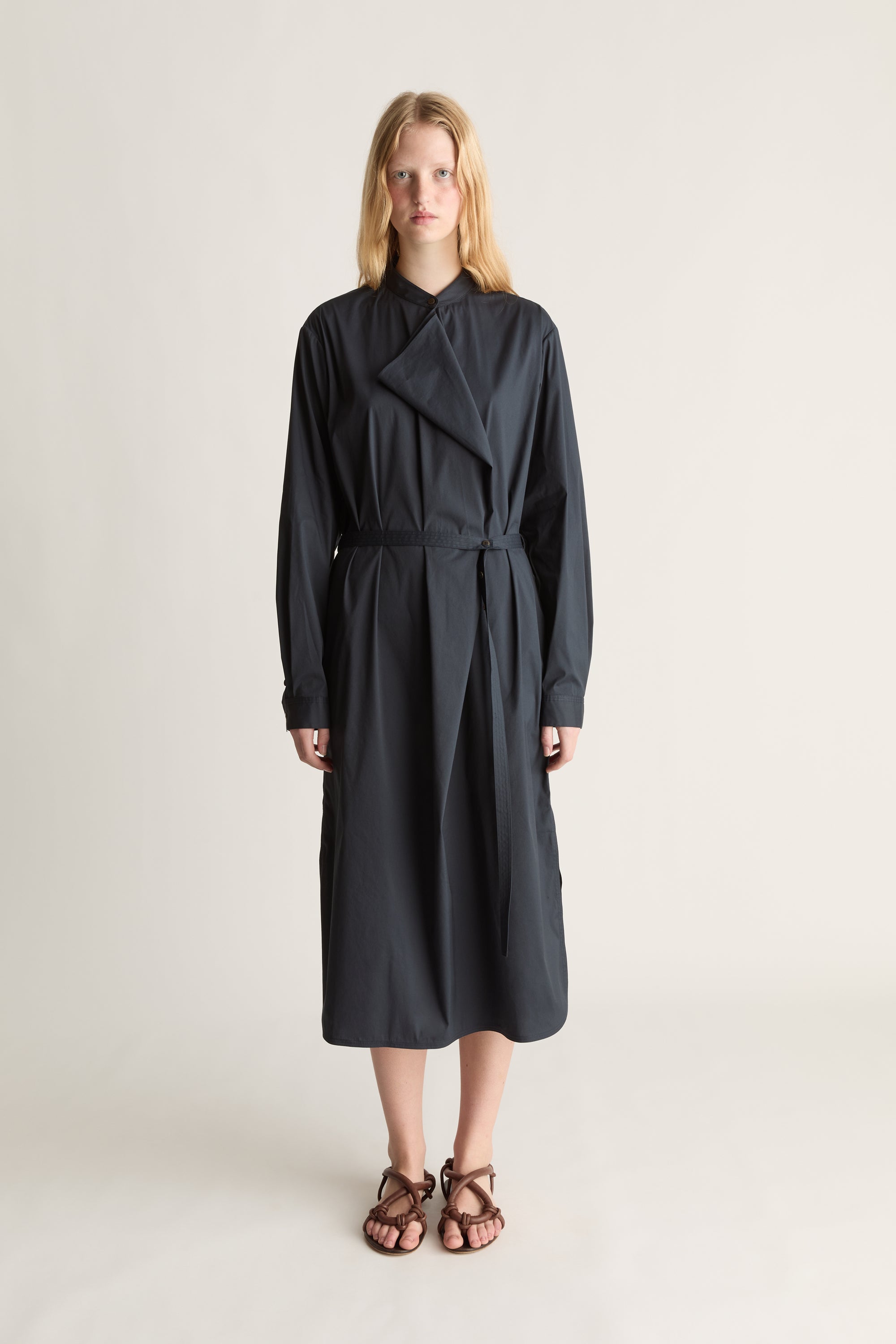 Front view of a model wearing a navy blue long sleeve shirt dress with a belted waist. Shot against a white studio background.