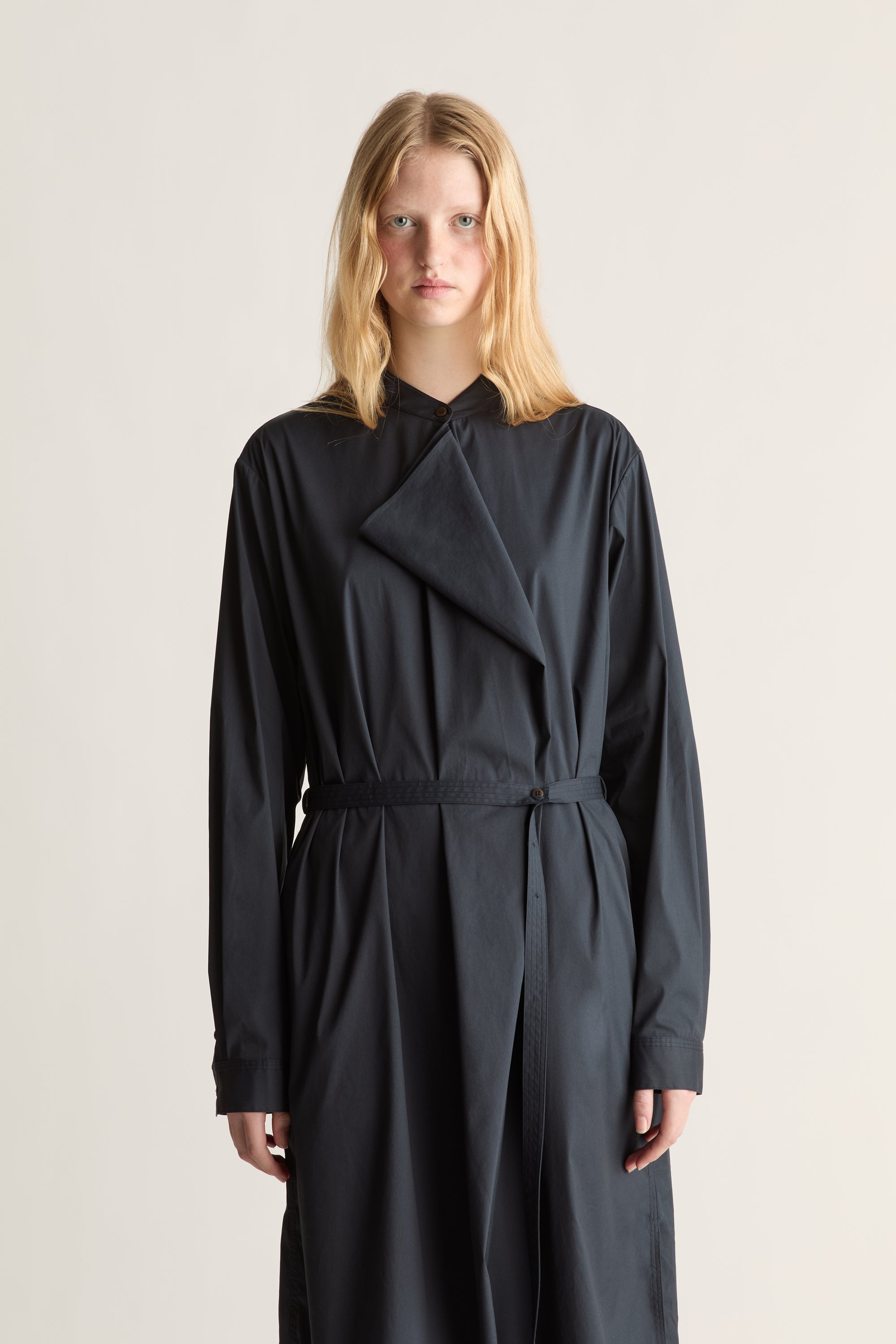 A model wearing a navy long-sleeve wrap-style dress with a tie waist, photographed against a plain light beige studio background.
