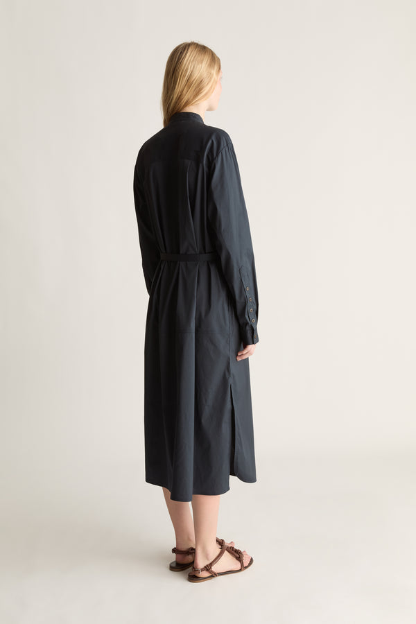 A woman shown from the back wearing a long dark navy midi shirt dress with a tie waist belt, paired with brown strappy flat sandals, against a plain light gray studio background.