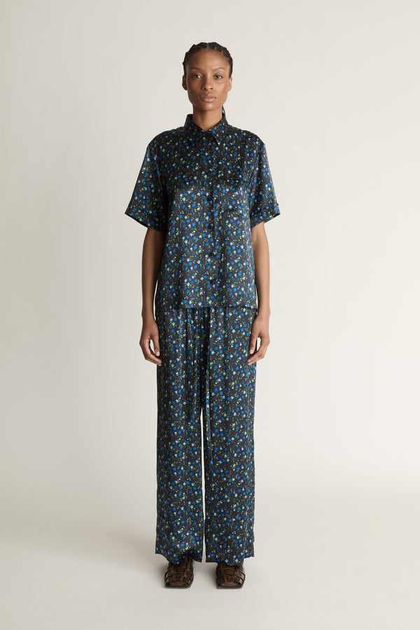 Person wearing a blue printed button-up shirt and pants on a plain background