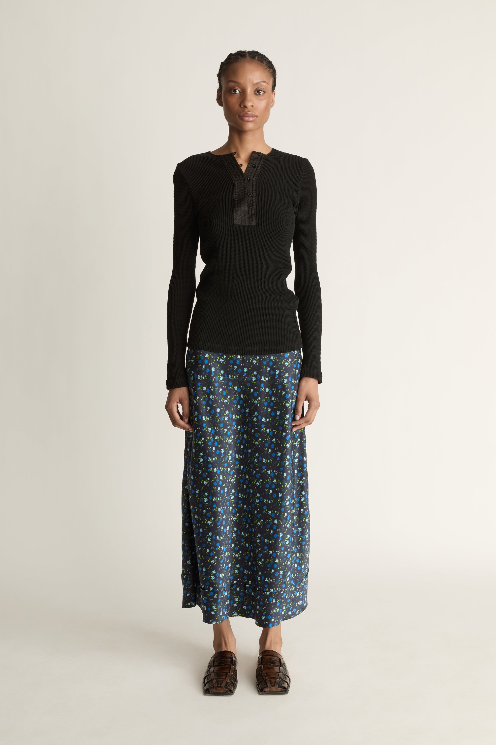 Woman wearing a black long-sleeve top and patterned skirt on a white background