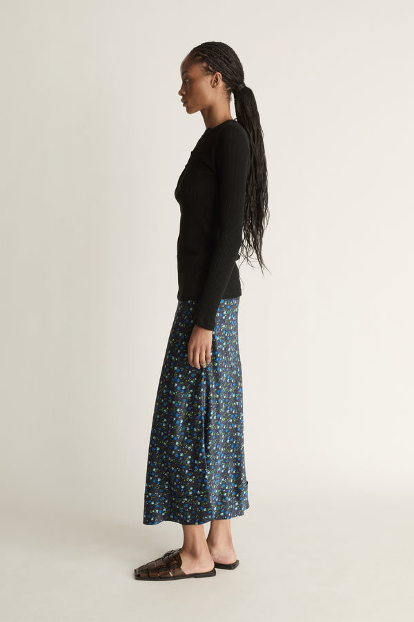 Woman wearing a black long-sleeve top and patterned skirt on a white background