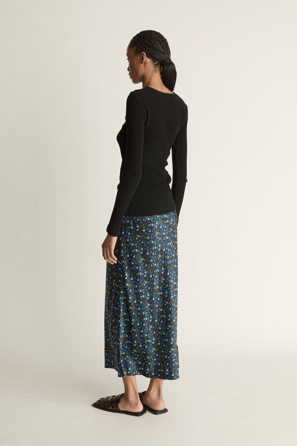 Woman wearing a black long-sleeve top and patterned skirt on a white background