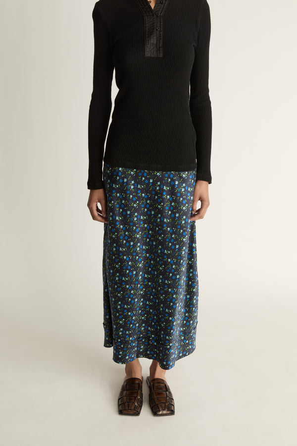 Woman wearing a black long-sleeve top and patterned skirt on a white background