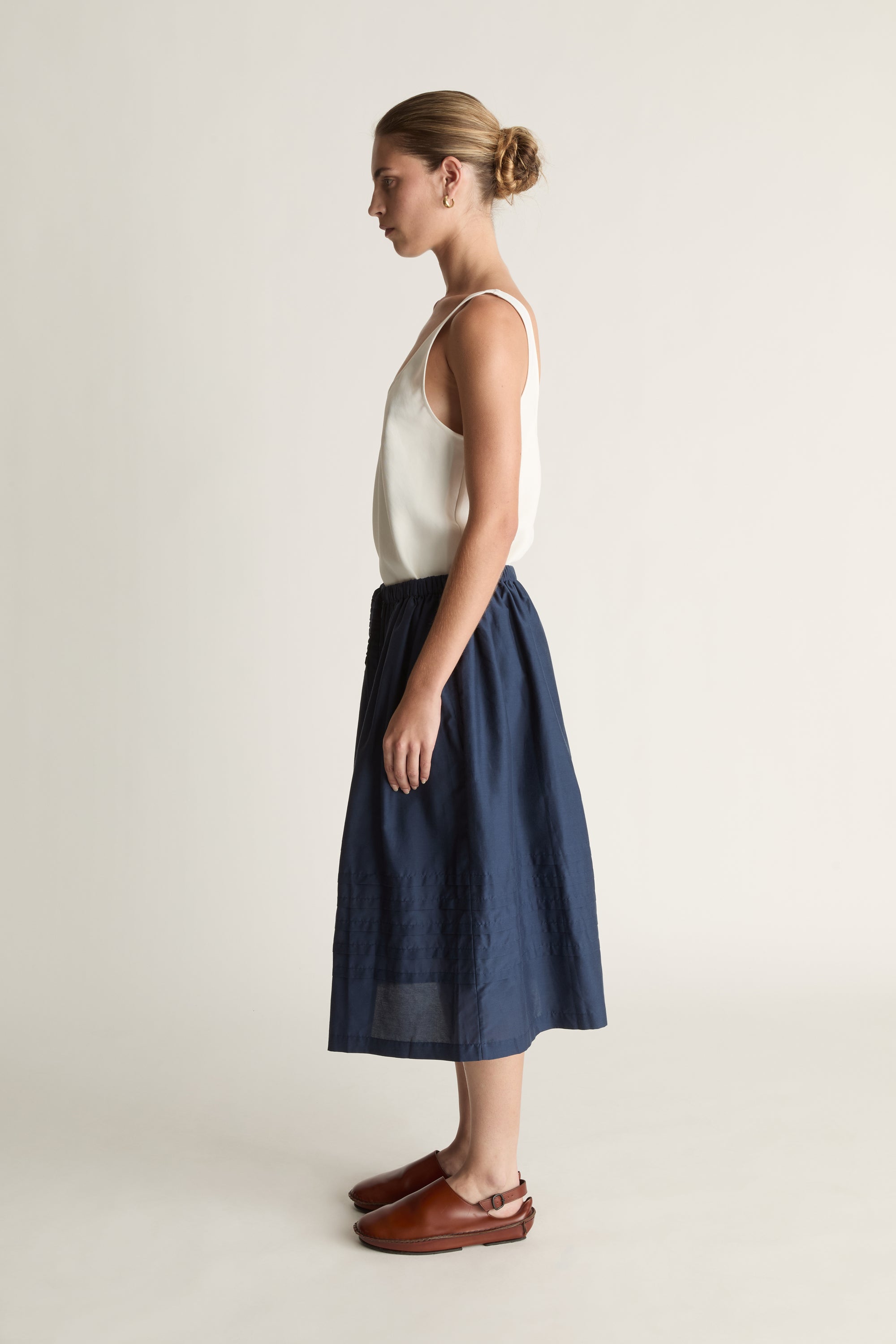 Woman wearing a white top and navy skirt on a plain background