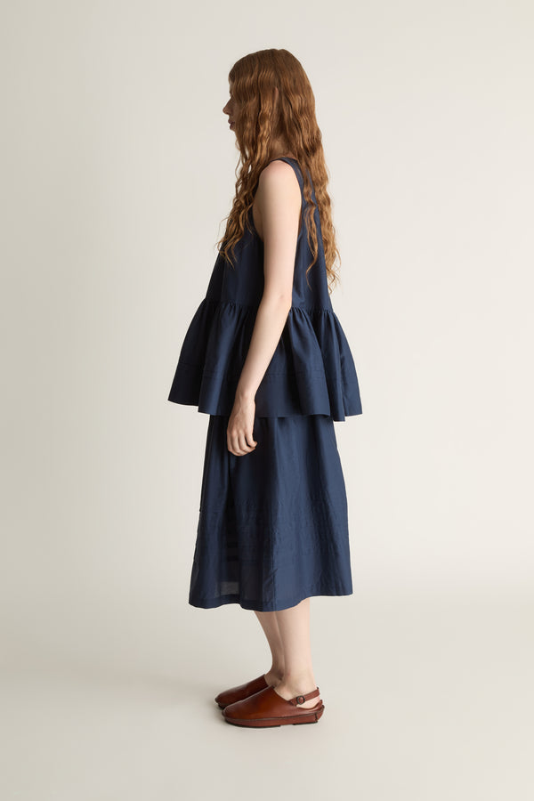 Woman wearing navy blue blouse with a gathered detail and a navy blue skirt on a white background