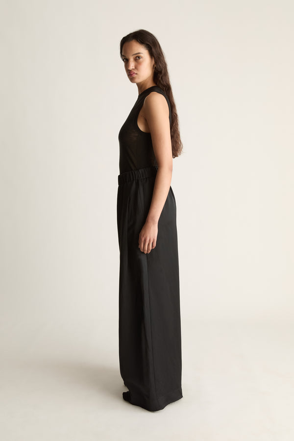 Side view of a woman looking over her shoulder in a black sleeveless top and black wide-leg pants
