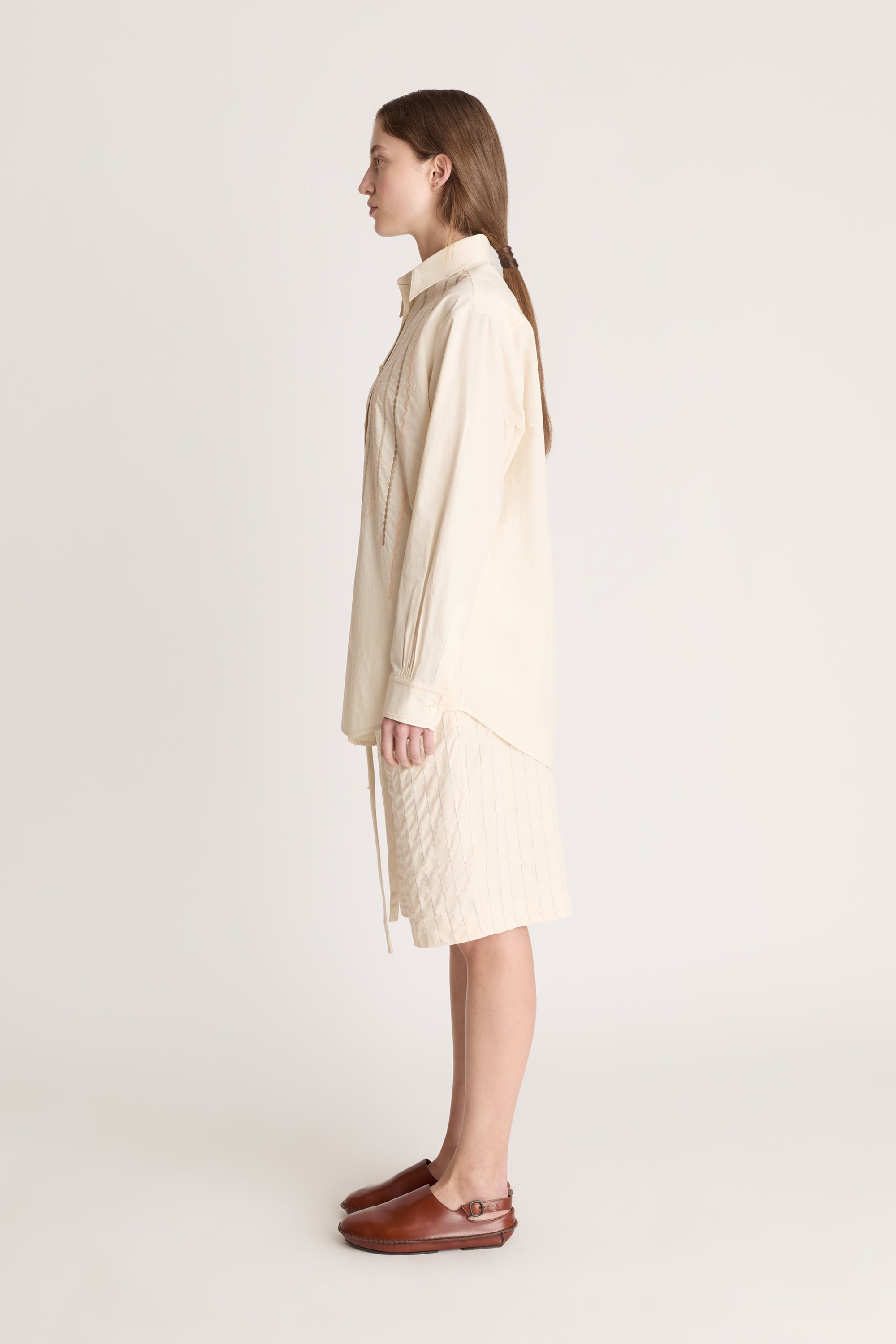 Woman wearing a beige  button up shirt with beige shorts on a white background.